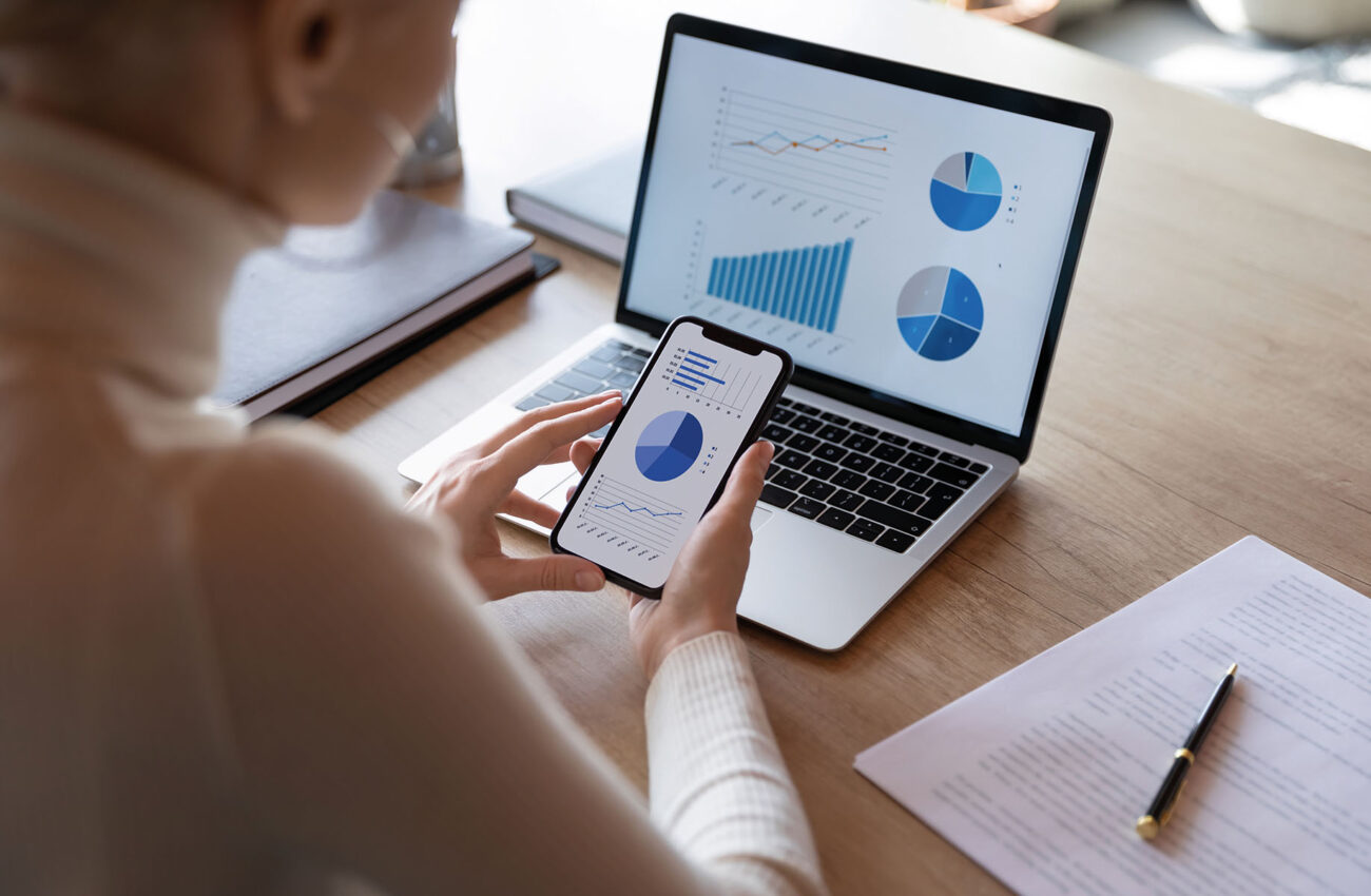 Businesswoman using smartphone and laptop, sales statistics on devices screens