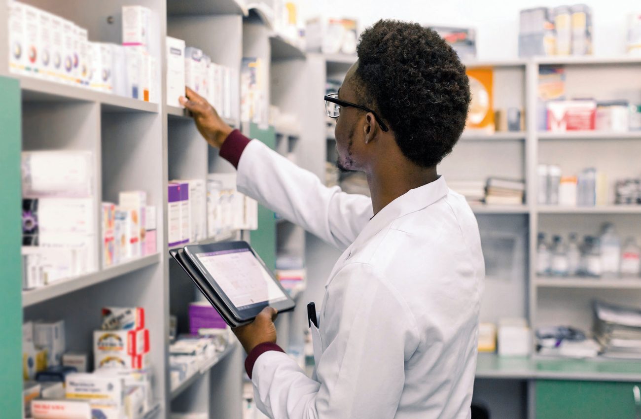 African American male pharmacist using digital tablet during inventory in pharmacy.